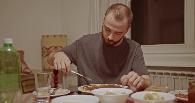 A young man meticulously prepares a sweet dessert, spreading rich chocolate onto a warm pancake and then sprinkling it with powdered sugar, creating a delicious homemade treat.