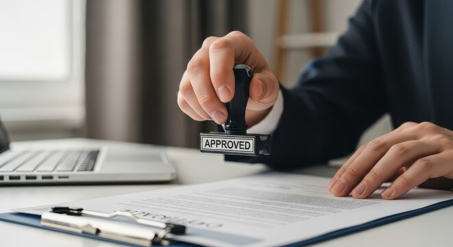 Close-up of a person's hand holding an 'Approved' stamp over a document