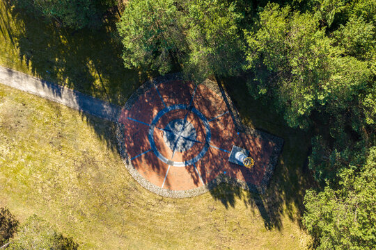 Aerial view of The Geographical Centre Of Europe monument featuring a large compass rose plaza and a white column with a golden crown surrounded by lush forest Girija, Vilnius County, Lithuania.