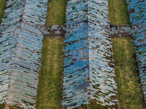 Aerial view of abandoned greenhouses with broken glass panels and overgrown green grass in Vilnius County, Lithuania.