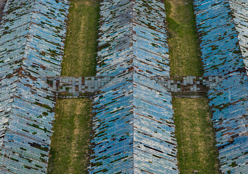 Aerial view of abandoned greenhouses with broken blue glass panels and rows of green grass in Vilnius County, Lithuania.
