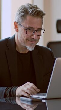 Business portrait - Businessman working with laptop computer talking on video call in meeting room of modern office. Happy middle aged, mid adult, mature age man smiling.