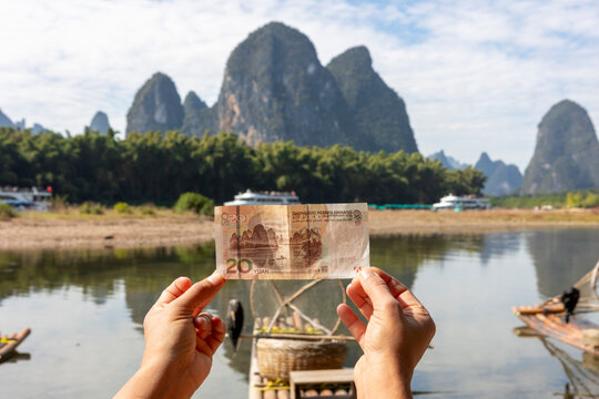Hands holding 20 yuan banknote aligning with Guilin karst mountains