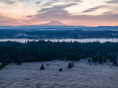 Aerial view of Mima Mounds Natural Area Preserve with Mount Rainier visible over a misty evergreen forest during a colorful sunrise Olympia, Washington, United States.