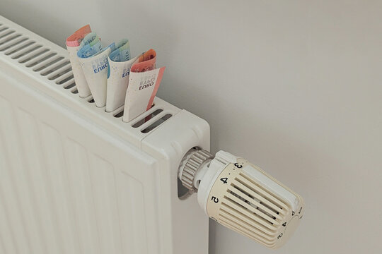 Closeup euros tucked in radiator near thermostat, symbol of rising heating costs, cold home mood