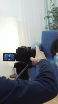 A camera is set up to capture a scene with a woman sitting on a blue couch. The camera operator adjusts the camera towards the woman for filming.