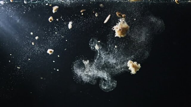 Pieces of brown dough falling into clear water creating bubbles and dissolving in slow motion