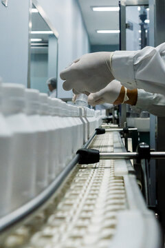 Close up of worker hands in white gloves inspecting plastic bottles on pharmaceutical production line