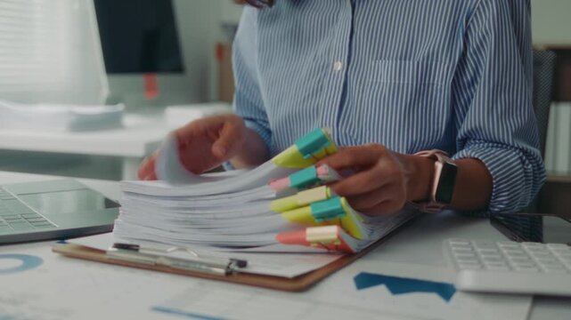 Close up of a female office worker hands searching for a specific document in a large pile of paperwork stacked on her office desk