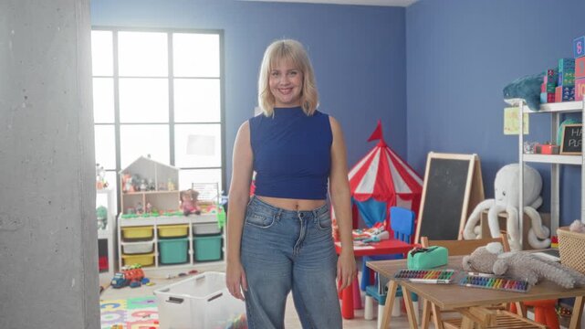 Woman standing smiling beside crayons and toys on a table in a colorful playroom building near a red tent and chalkboard; playful joy.