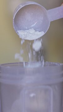 Close up of whey protein powder pouring from scoop into shaker bottle for fitness supplement video in vertical 4k.
