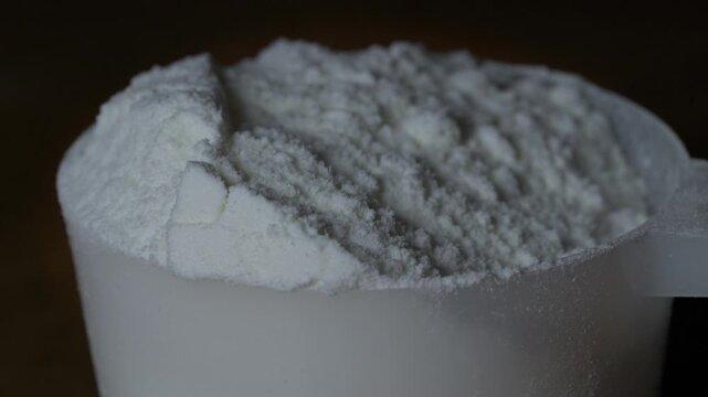 Macro close up of white powder in plastic scoop for protein collagen supplement nutrition or food ingredient concept.