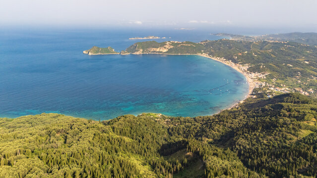 Scenic drone aerial view in light haze on Akra Arilla, cape Arilla and Agios Georgios Pagon beach on Corfu island in sunny summer day. Colorful view over Ionian Sea, beach and rocky cliffs.