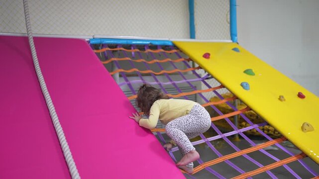 A child climbing on a colorful mat. Girl, child, climbs, playroom, development, fine motor skills. A young girl develops fine motor skills. Describe lifestyle.