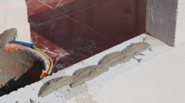 The worker lays a mixture of cement and sand on top of the white brick