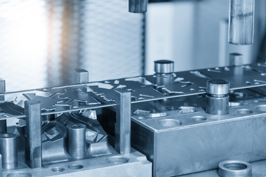 Industrial operation of a progressive die forming high-precision sheet metal parts in a blue-toned scene with lighting effects.