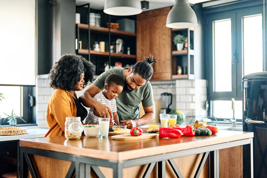 Portrait of mother, father and son preparing and eating breakfast in the kitchen at home