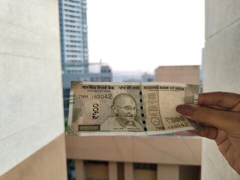 Indian 500 Rupee Banknote Held Against Urban Balcony View