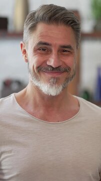 Portrait of happy, confident older man at home looking at camera smiling. Mature age, middle age, mid adult casual guy in 50s, bearded, gray hair.