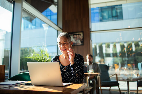 Senior woman on video call with laptop in modern cafe