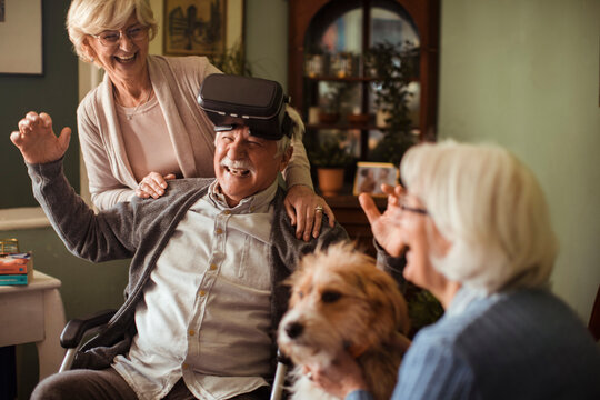 Senior man in wheelchair enjoying virtual reality with friends at home