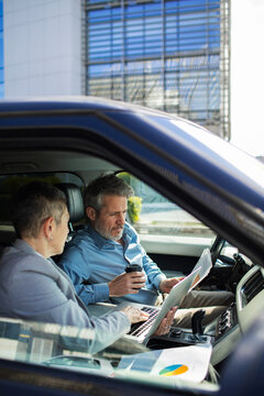 Business colleagues reviewing reports in car outside office