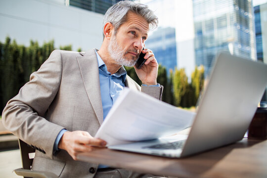 Mature businessman on phone with documents and laptop outside office