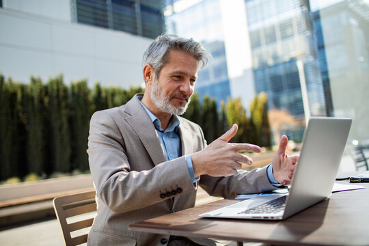Mature businessman on laptop video call at outdoor office