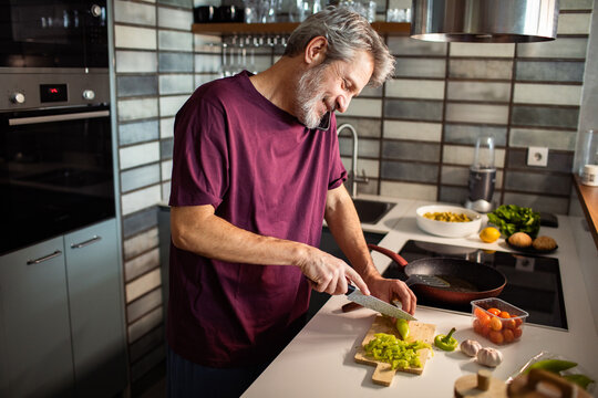 Middle-aged man chopping vegetables while talking on phone in home kitchen