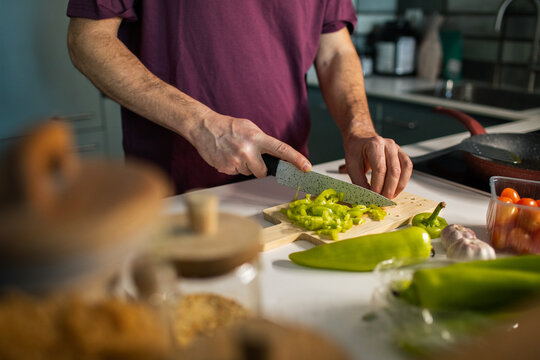 Man slicing green bell pepper on cutting board in home kitchen