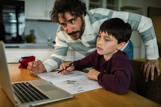 Father helping son with homework at home kitchen table