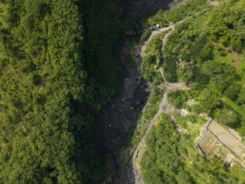 Aerial view of Tambang Pasir Merapi Kali Gendol Sand Mine with excavators and trucks in the riverbed surrounded by forest Kecamatan Cangkringan, Daerah Istimewa Yogya, Indonesia.