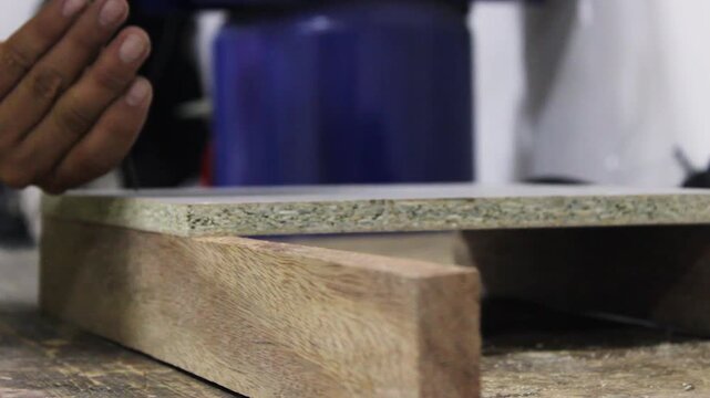 An unrecognizable person is using a cordless electric drill to drive a metal screw into a board inside a carpentry workshop in Neiva, Huila, Colombia. Concept of handmade and industry