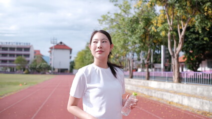 Fototapeta premium Female athlete taking a break outdoors, drinking water, with water bottom, Happy sportswoman taking a water break outdoors