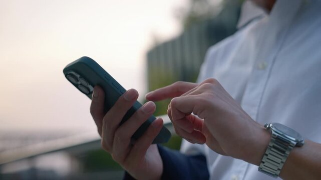 Close up of young businessman using smartphone with one hand while standing outdoors in modern urban office environment. Mobile technology and digital communication concept.
