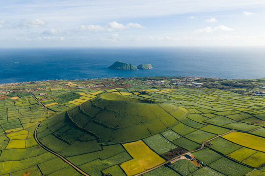 Aerial view of Pico Dona Joana volcanic cone surrounded by green patchwork fields and stone walls overlooking the Atlantic Ocean Feteira, Acores, Portugal.