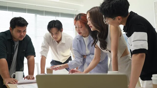 Group of Young Asian Business Professionals Brainstorming and Analyzing Data Charts in Modern Office Team Collaboration on Financial Growth and Marketing Strategy Concept