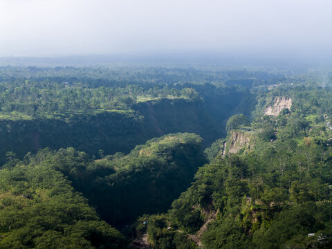 Aerial view of Tambang Pasir Merapi Kali Gendol Sand Mine surrounded by dense tropical forest and steep cliffs under a hazy sky Kecamatan Cangkringan, Daerah Istimewa Yogya, Indonesia.