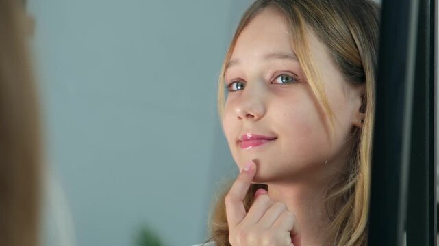 A little girl or teenager aged 10-12 looks with admiration at her reflection in the mirror and admires her appearance. Acceptance of one's appearance, healthy self-esteem.