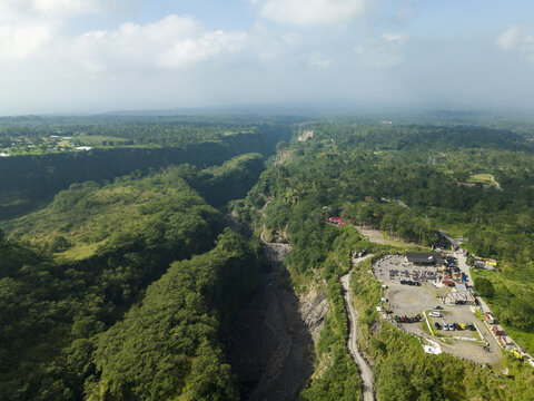 Aerial view of Tambang Pasir Merapi Kali Gendol Sand Mine with deep river valley surrounded by lush green forest and parking area Kecamatan Cangkringan, Daerah Istimewa Yogya, Indonesia.