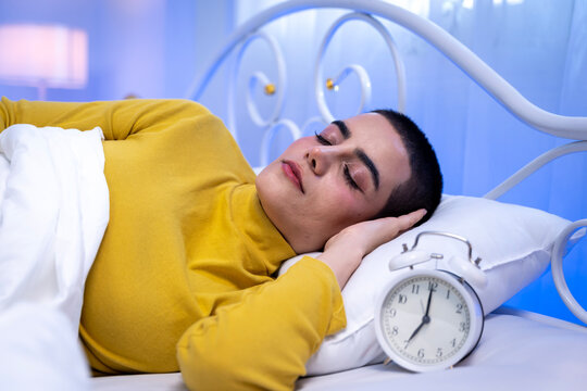 Young short haired woman sleeping in bed and reaching to turn off alarm clock in the morning