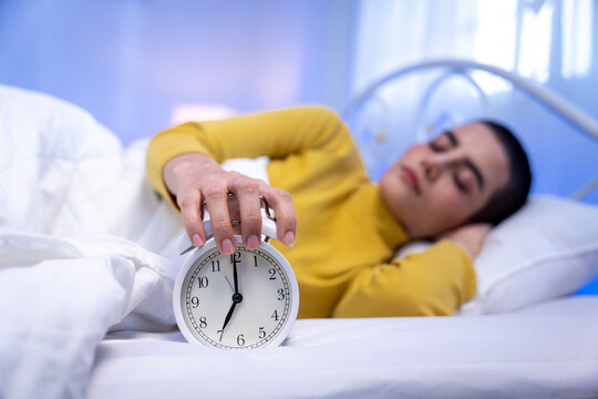 Young short haired woman sleeping in bed and reaching to turn off alarm clock in the morning