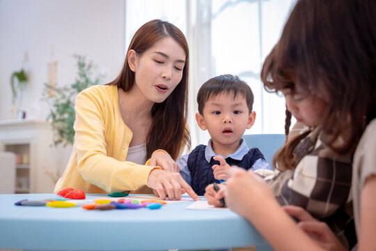Asian teacher teaching little children to draw and color with crayons in classroom at preschool