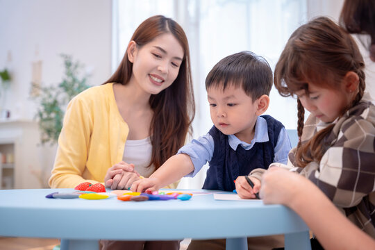 Asian teacher teaching little children to draw and color with crayons in classroom at preschool