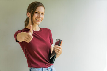 Fototapeta premium Happy young woman holding digital tablet and showing thumbs up gesture against grey background.