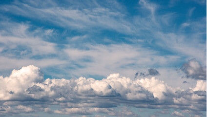 Obraz premium Cielo azul con nubes blancas y grises de tipo cúmulo, esponjosas y dispersas, creando una atmósfera tranquila y luminosa con tonos suaves y contrastes naturales.