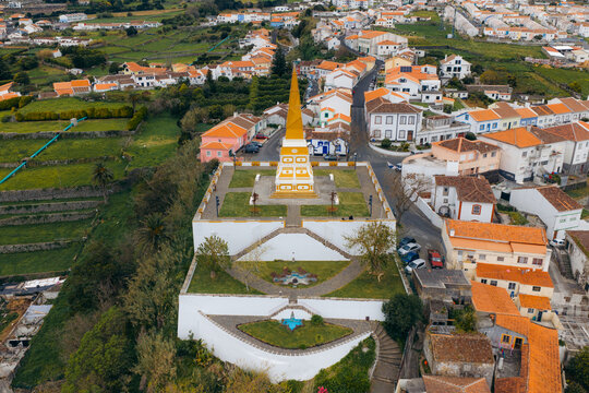 Aerial view of the Alto da Memoria obelisk with its yellow and white facade overlooking terraced gardens and the historic town of Angra do Heroismo, Azores, Portugal.