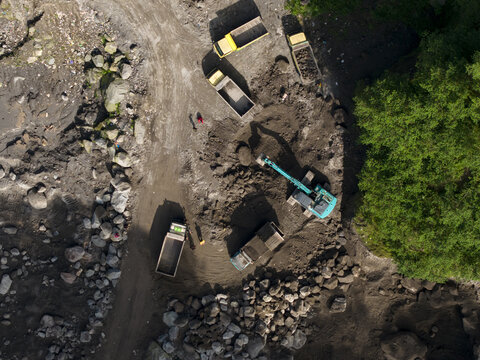Aerial view of Tambang Pasir Merapi Kali Gendol Sand Mine with an excavator loading trucks and workers on the ground in Kecamatan Cangkringan, Daerah Istimewa Yogya, Indonesia.