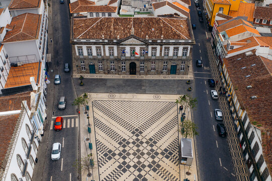 Aerial view of the historic town hall and the patterned cobblestone square of Praca Velha surrounded by traditional buildings in Angra do Heroismo, Azores, Portugal.