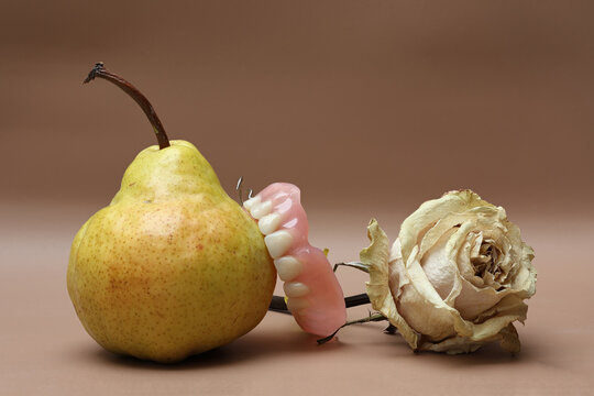 Still life of teeth biting into pear with dry rose looks on. Photo with great depth of field on light brown background.